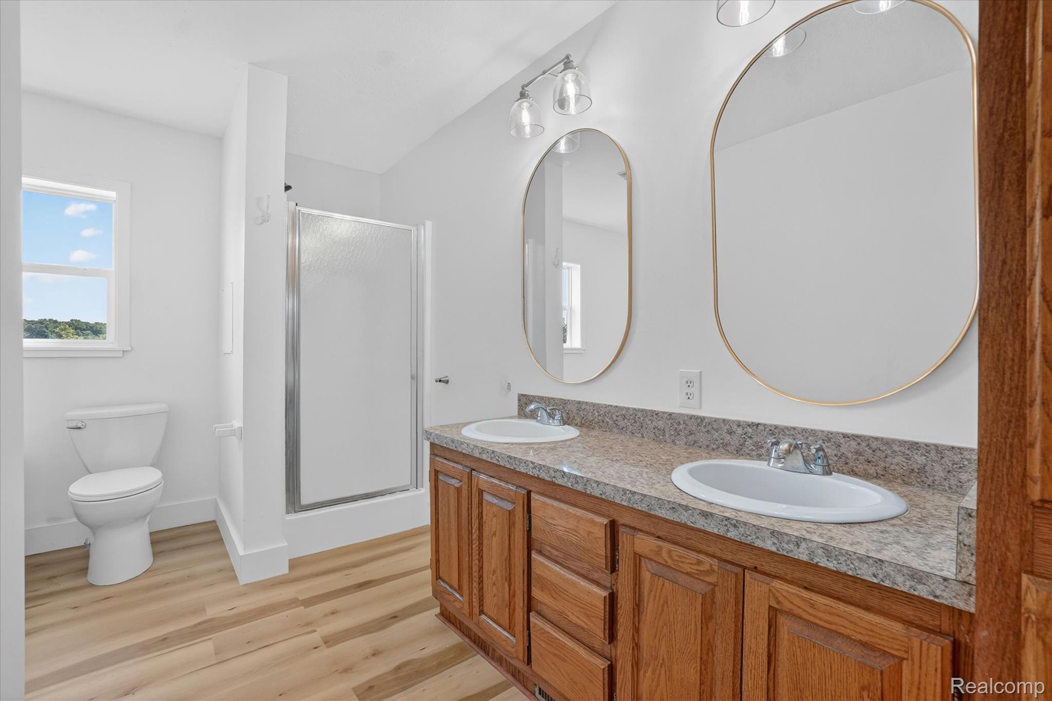 1400 North Every Road Mason, MI 48854 - Photo 15 of 33 Dual vanity with a stone-look countertop, two oval mirrors, and light wood-finish flooring