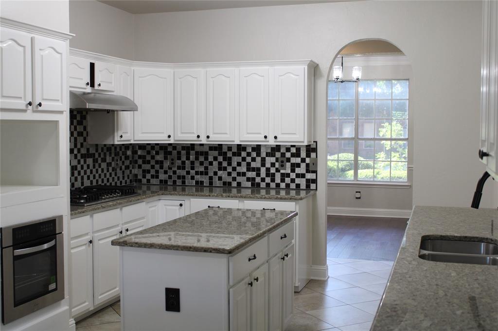 8905 Lakepointe Avenue Rowlett, TX 75088 - Photo 12 of 27 Kitchen with stainless steel appliances, tasteful backsplash, light stone countertops, white cabinetry, and a center island