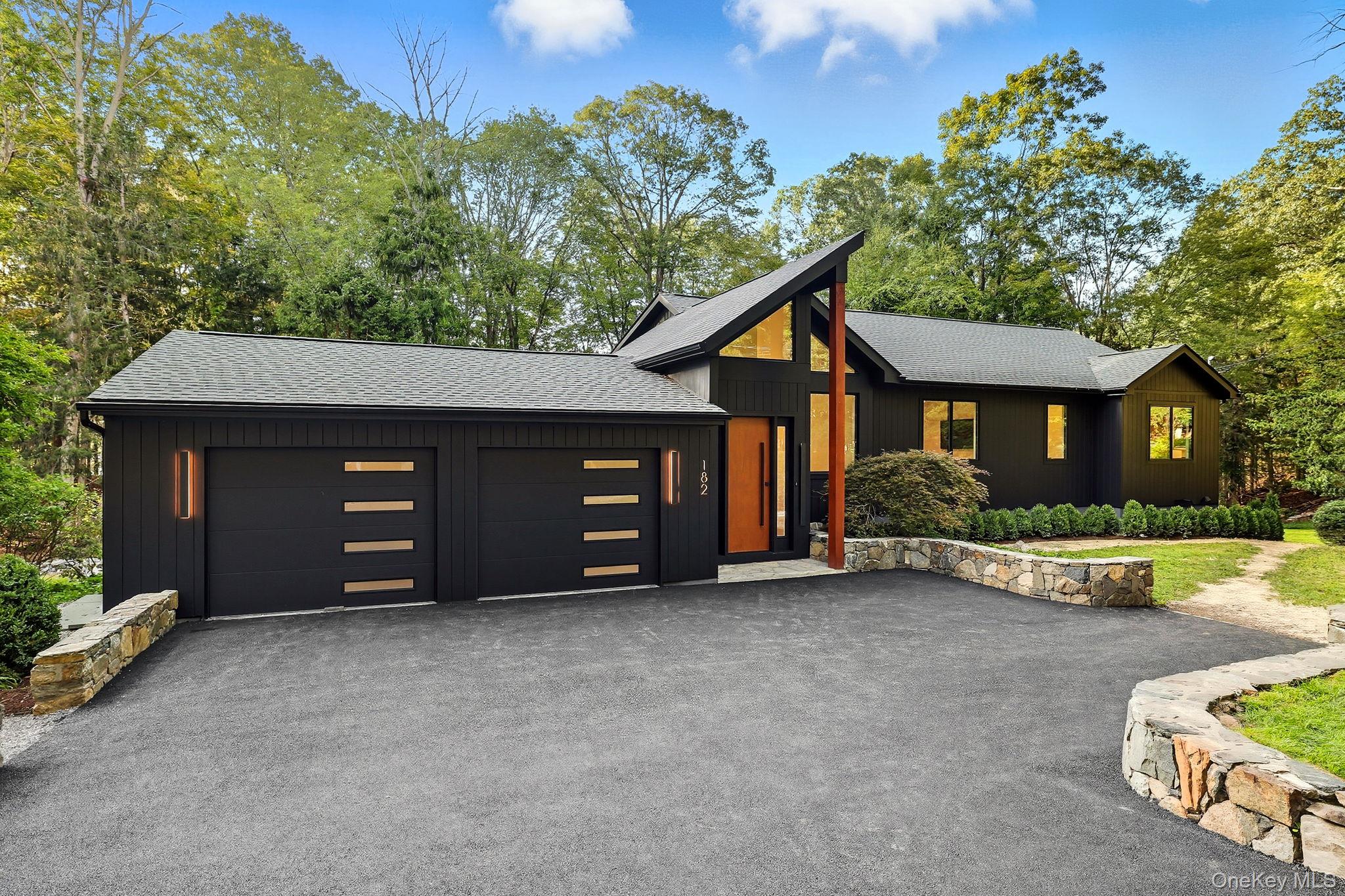 View of front of home featuring roof with shingles, asphalt driveway, an attached garage, and view of scattered trees