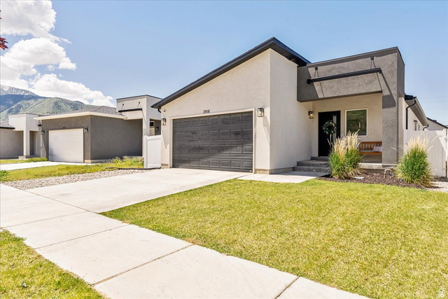 3916 South Sage Wood Avenue Mapleton, UT 84664 - Photo 4 of 33 Contemporary stucco exterior featuring a dark gray garage door, a covered entry, and a manicured lawn