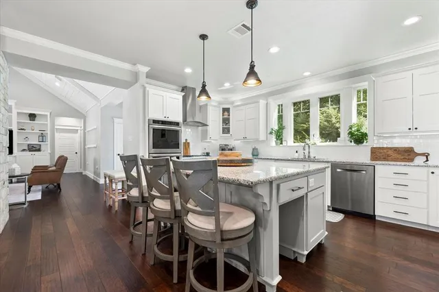 a kitchen with stainless steel appliances kitchen island granite countertop a wooden floor and white cabinets