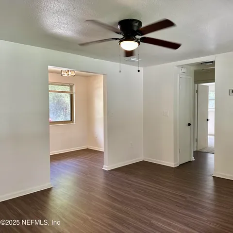 an empty room with wooden floor chandelier fan and windows