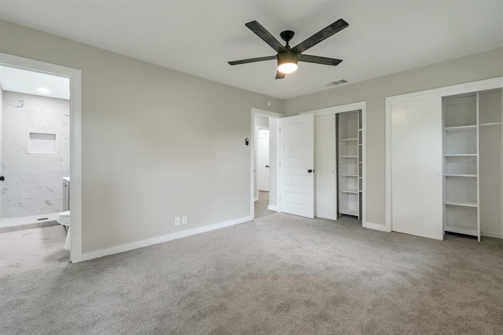 4815 Kelman Street Dallas, TX 75214 - Photo 23 of 37 Carpeted bedroom featuring a ceiling fan with integrated lighting, two built-in closet storage systems, a white shaker-style door with matte black hardware, and an en-suite bathroom with marble-look tile flooring and shower surround
