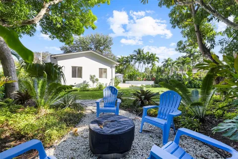 a view of a backyard with table and chairs potted plants and large tree