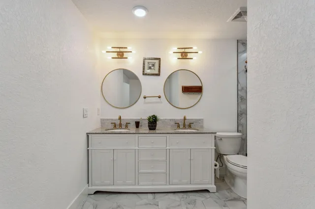 a bathroom with a toilet a double vanity sink and a mirror