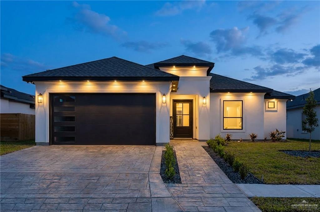 Prairie-style house with stucco siding, a shingled roof, decorative driveway, and a garage