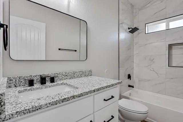 a bathroom with a granite countertop sink a toilet mirror and bathtub