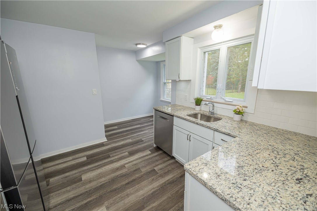 Kitchen featuring tasteful backsplash, dark wood-type flooring, light stone counters, and white cabinetry