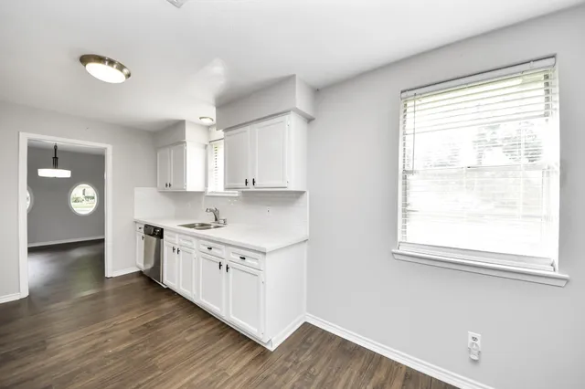 a kitchen with granite countertop a stove a sink and white cabinets with wooden floor next to windows