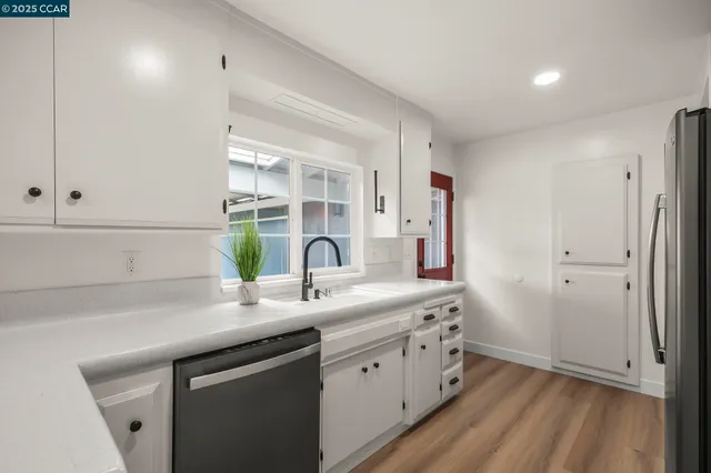 a kitchen with stainless steel appliances kitchen island granite countertop a refrigerator a stove a sink dishwasher and white cabinets with wooden floor