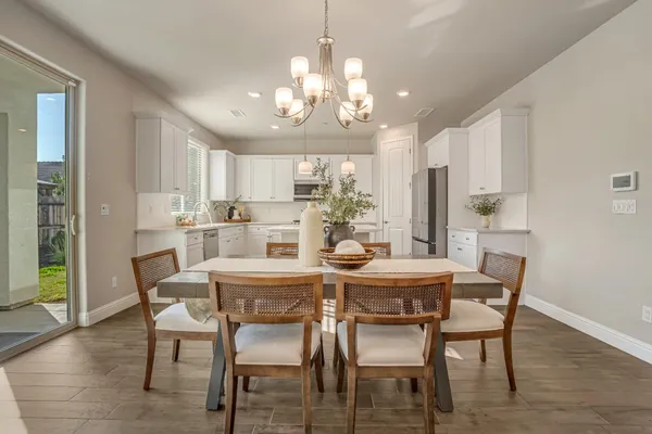 a kitchen with stainless steel appliances kitchen island granite countertop a refrigerator a stove a dining table and chairs with wooden floor