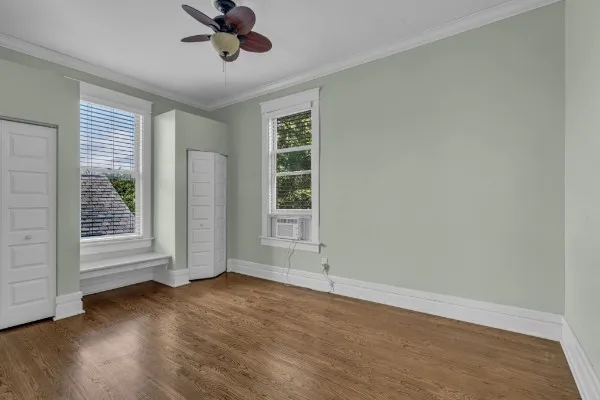 an empty room with wooden floor chandelier fan and windows