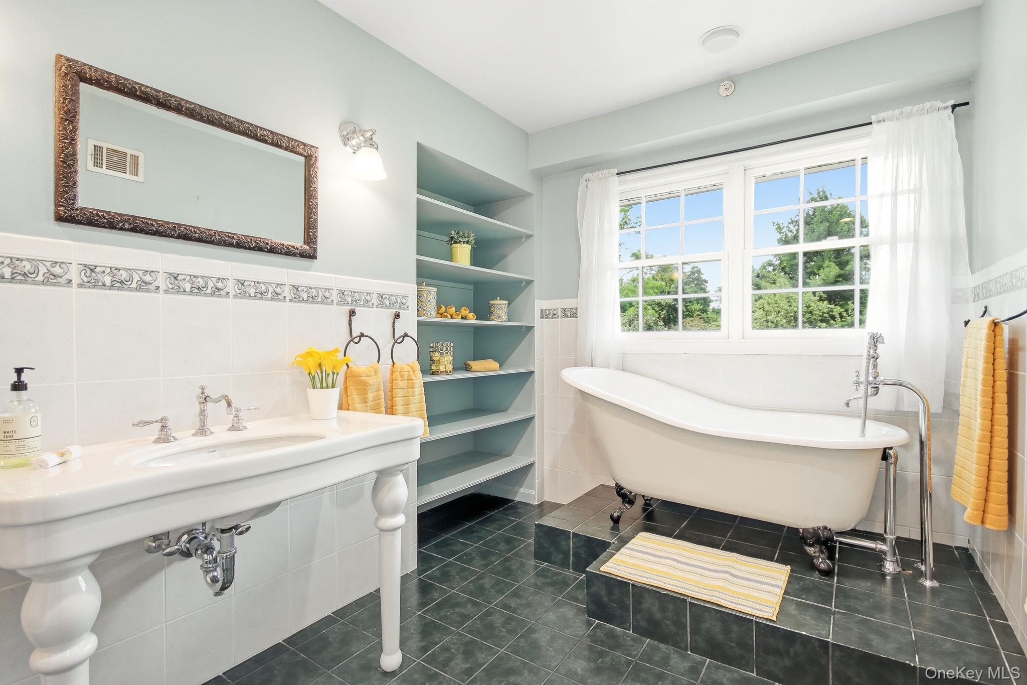 26 Century Ridge Road Purchase, NY 10577 - Photo 17 of 50 Primary en-suite bathroom featuring a freestanding clawfoot tub, a pedestal sink with chrome fixtures, built-in shelving, white tiled wainscoting with decorative trim, and dark tile flooring