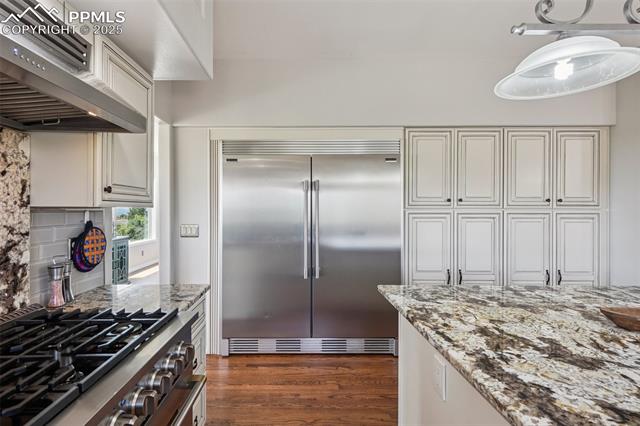14425 Granby Road Colorado Springs, CO 80921 - Photo 15 of 45 Kitchen with appliances with stainless steel finishes, wall chimney range hood, dark wood-type flooring, backsplash, and light stone countertops