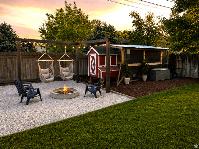 1791 West 170 South, Unit 8 Provo, UT 84601 - Photo 25 of 25 Expansive backyard featuring a gravel patio with a concrete fire pit, a wooden pergola with hanging hammock chairs, a manicured lawn, a wooden privacy fence, and a red chicken coop structure with an attached enclosure