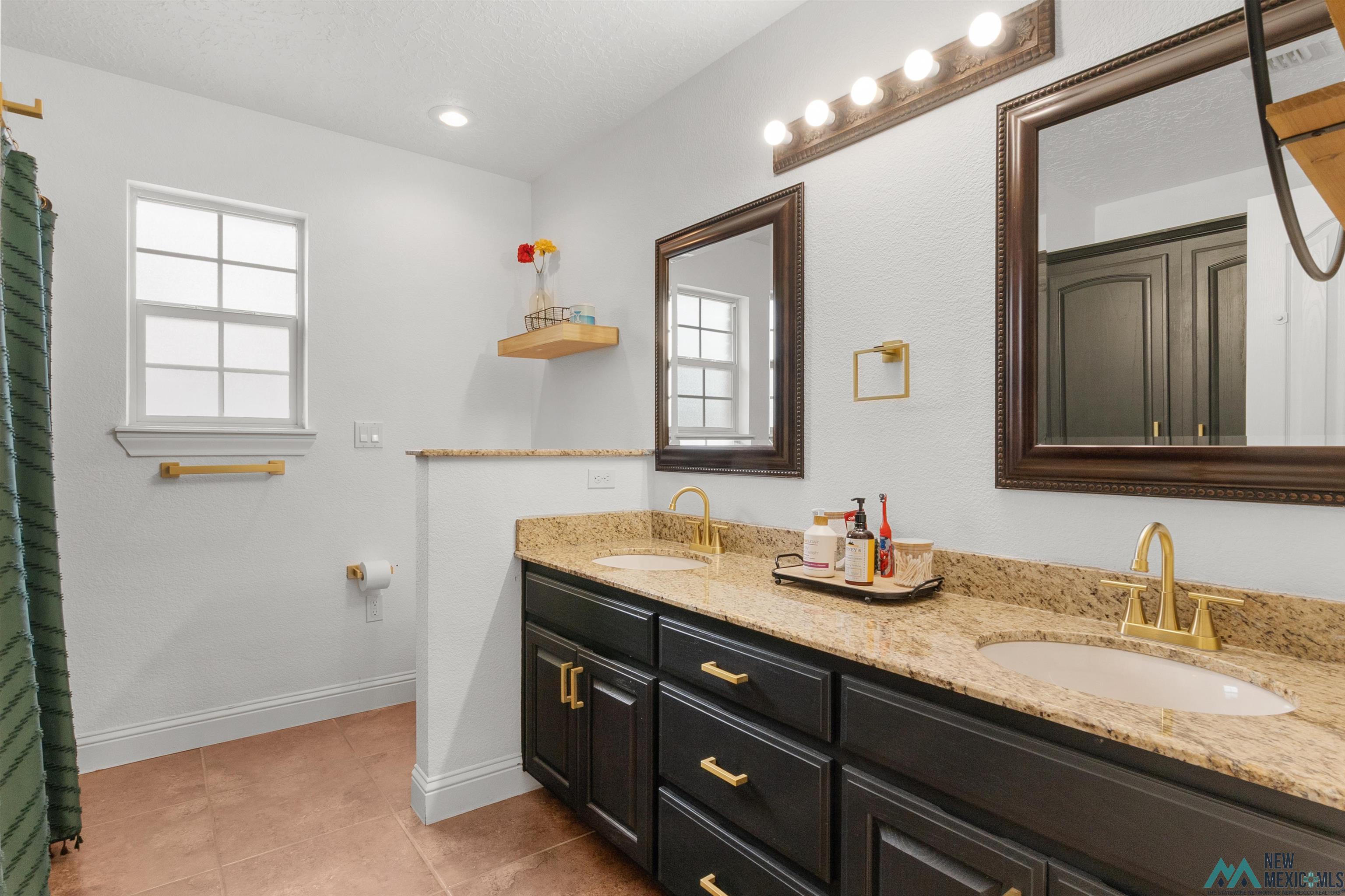 3913 Woodlark Road Clovis, NM 88101 - Photo 24 of 28 Double vanity featuring dark wood cabinetry, granite countertops, and gold-finish fixtures