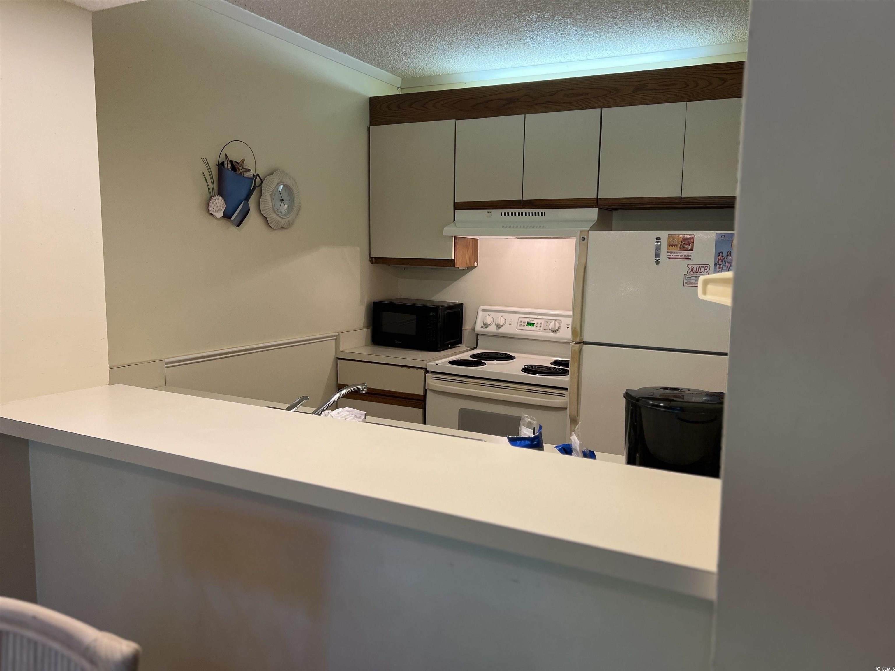 415 Ocean Creek Drive, Unit 2188 Myrtle Beach, SC 29572 - Photo 7 of 28 Kitchen with white appliances, a textured ceiling, light countertops, under cabinet range hood, and ornamental molding