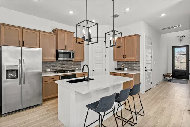 a kitchen with stainless steel appliances a stove a sink a refrigerator a center island a wooden floor and white cabinets