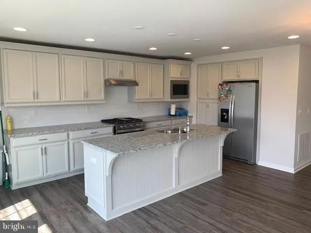 a kitchen with stainless steel appliances granite countertop a refrigerator a sink dishwasher a stove and white cabinets with wooden floor