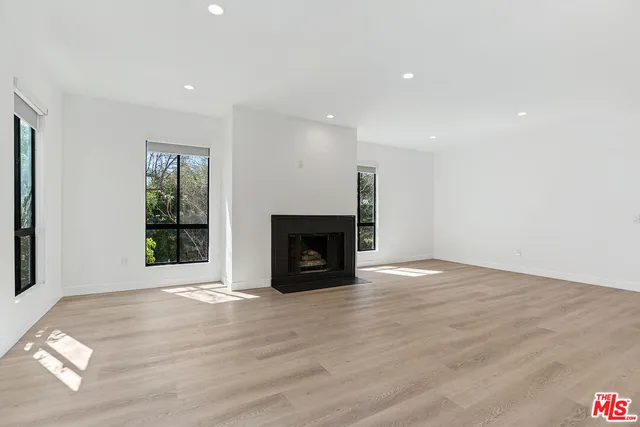 a view of an empty room with wooden floor fireplace and a window