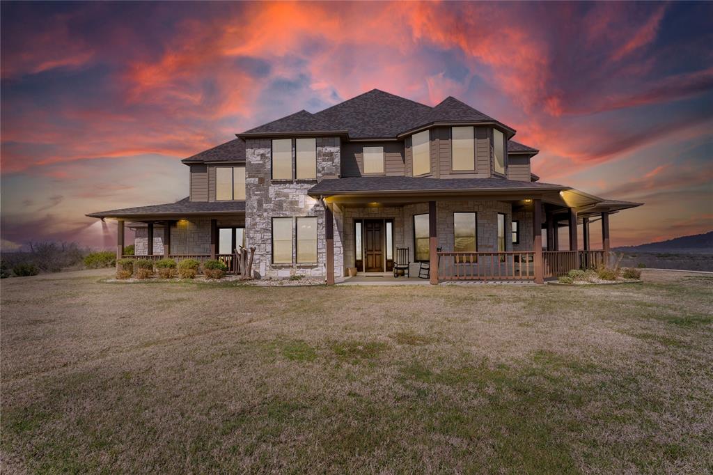 View of front of home featuring stone siding, a lawn, and covered porch