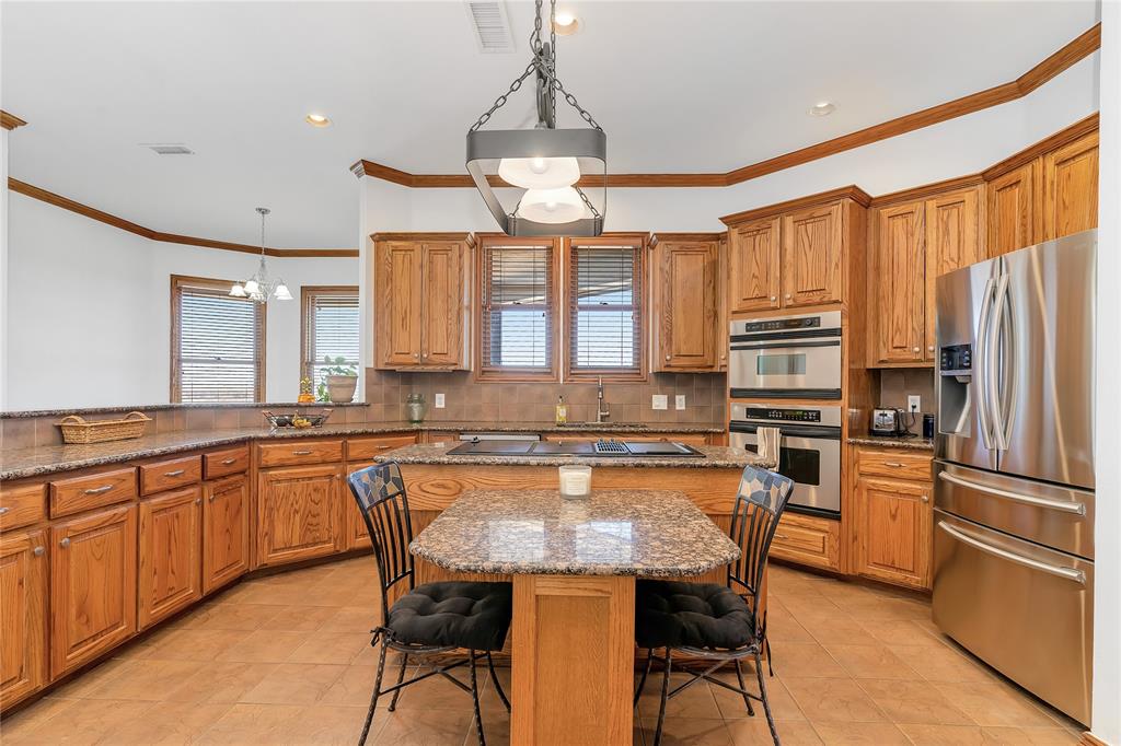 4520 South Nolan River Road Cleburne, TX 76033 - Photo 12 of 40 Kitchen featuring a kitchen breakfast bar, a center island, appliances with stainless steel finishes, decorative backsplash, and a chandelier