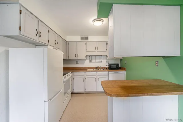 a kitchen with granite countertop a white refrigerator oven a sink dishwasher and white cabinets with wooden floor