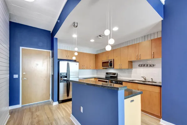 a kitchen with stainless steel appliances granite countertop a refrigerator a stove and a sink with wooden floor