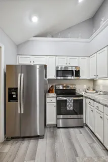 a kitchen with stainless steel appliances granite countertop a sink a stove oven a refrigerator with white cabinets and wooden floor