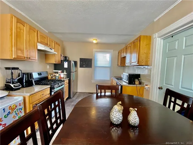 a kitchen with stainless steel appliances granite countertop a stove top oven a refrigerator a dining table and chairs with wooden floor