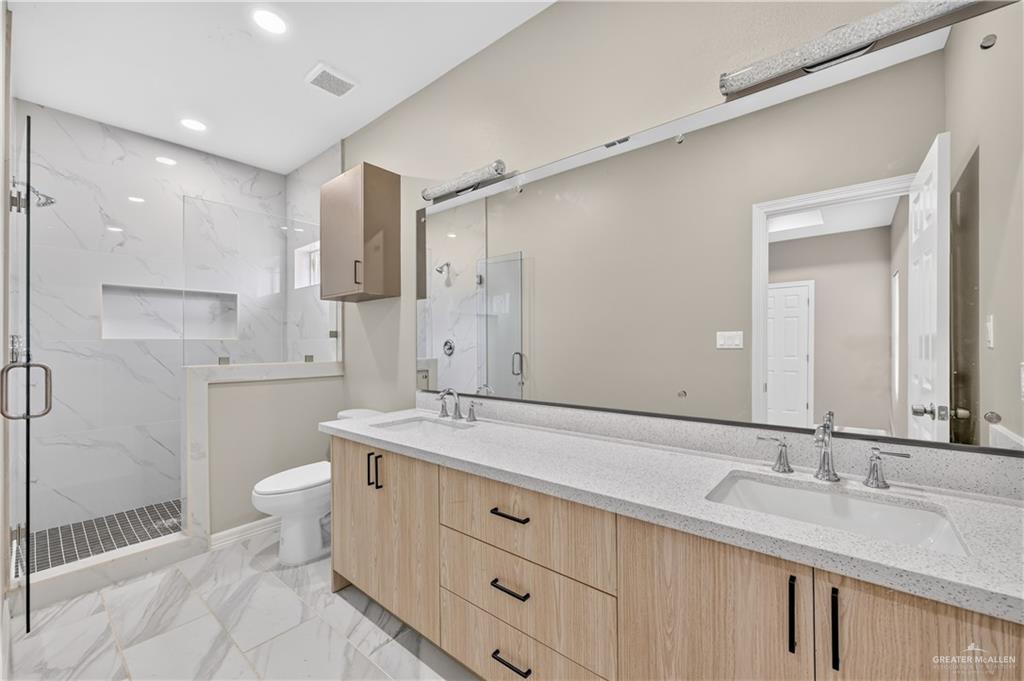 1920 Trinity Street Donna, TX 78537 - Photo 15 of 23 Contemporary bathroom featuring a spacious glass-enclosed shower with subway tile, dual vanity with light wood-finish cabinetry, quartz countertops, and a full-width mirror