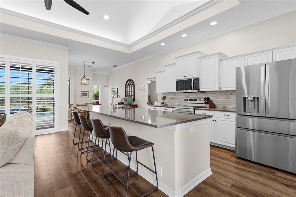 6582 Waters Edge Way Lakewood Ranch, FL 34202 - Photo 16 of 98 a kitchen with stainless steel appliances granite countertop a refrigerator a stove top oven a sink dishwasher a dining table and chairs with wooden floor