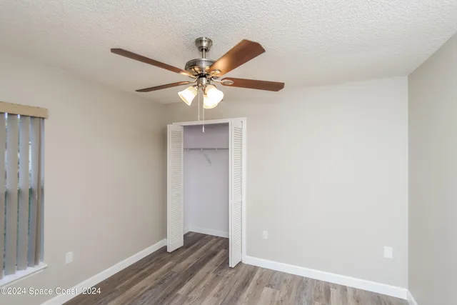 an empty room with wooden floor fan and windows