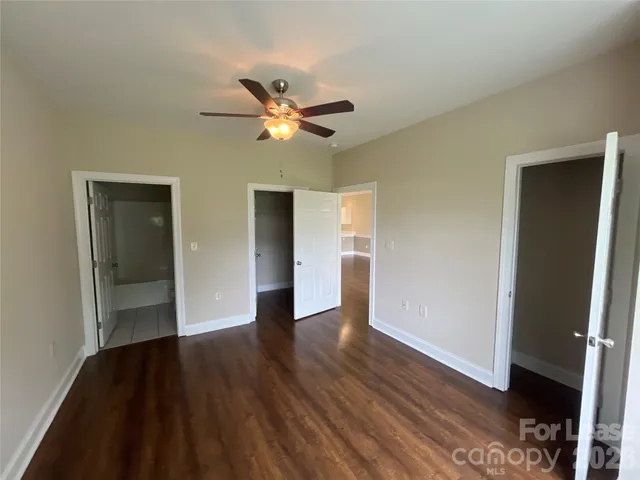 a view of an empty room with wooden floor and a ceiling fan