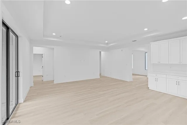 a view of an empty room with kitchen and window