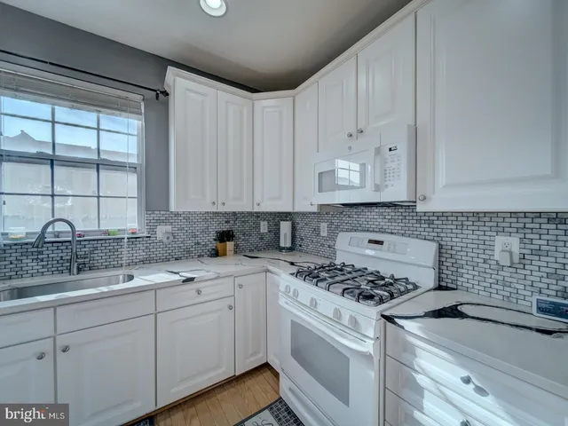 a kitchen with a sink dishwasher a stove and white cabinets with wooden floor