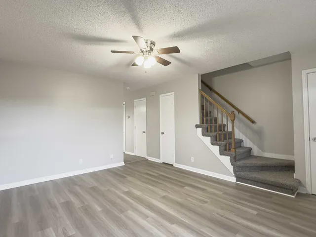 a view of an empty room with wooden floor and a ceiling fan