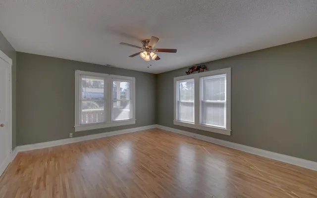 a view of empty room with wooden floor and fan