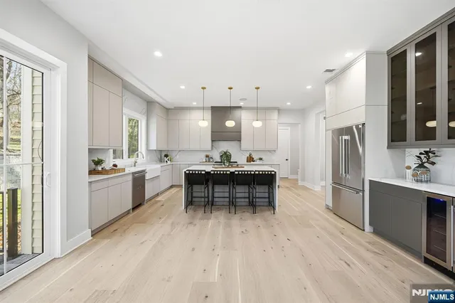 a large white kitchen with a refrigerator a sink dishwasher a dining table and chairs with wooden floor