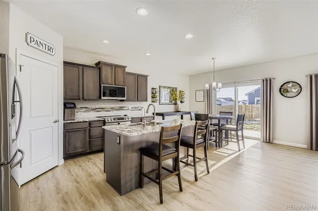 a kitchen with stainless steel appliances granite countertop a stove top oven a refrigerator a dining table and chairs with wooden floor