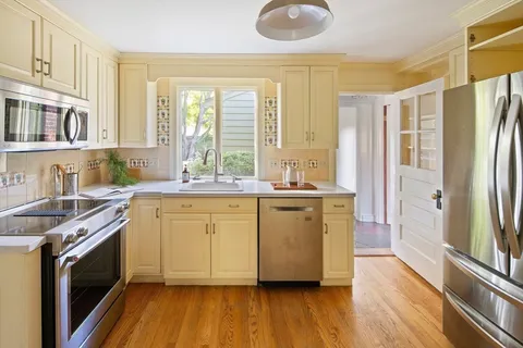 a kitchen with stainless steel appliances granite countertop a refrigerator a sink dishwasher a stove and white countertops with wooden floor