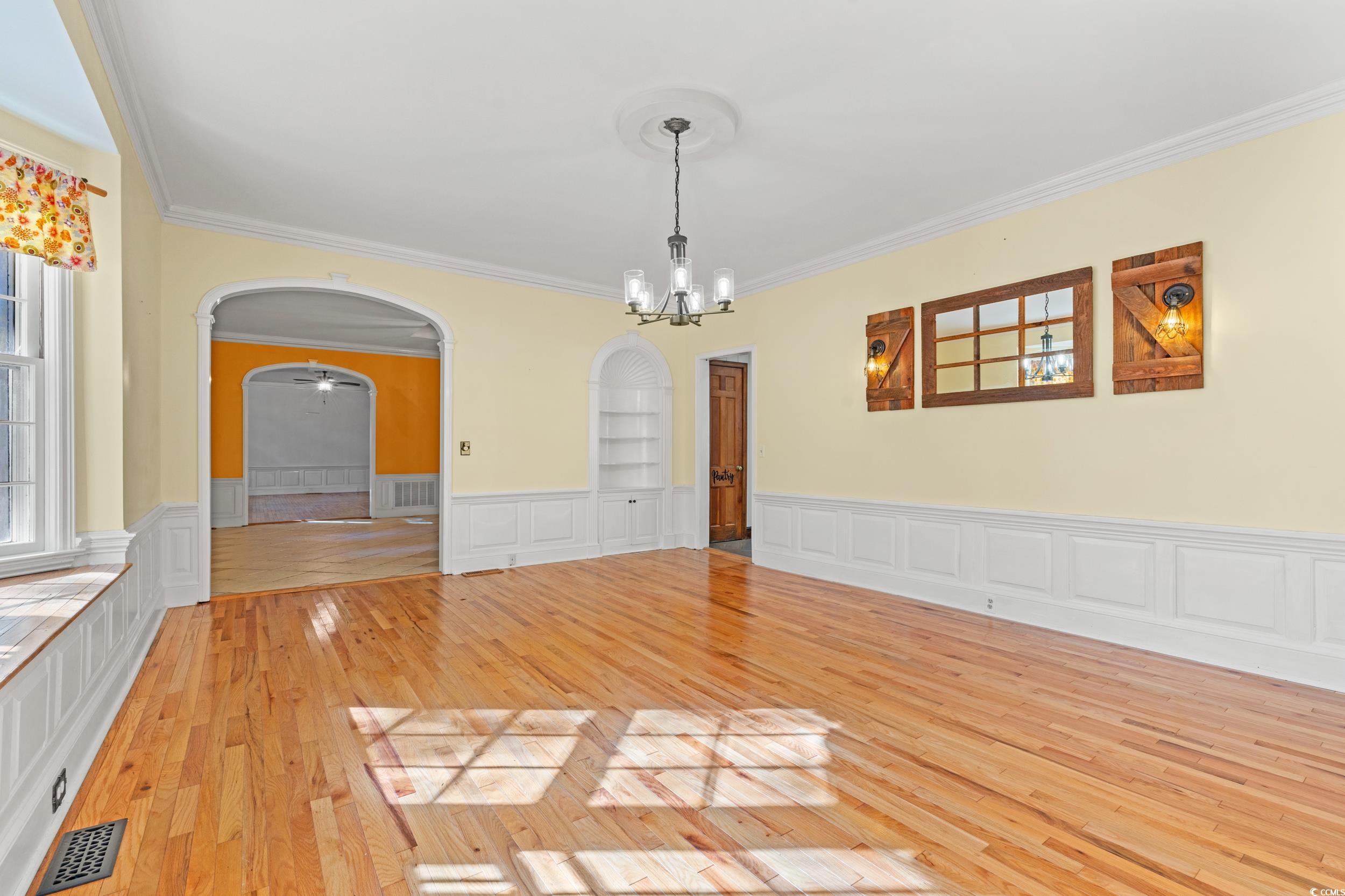 607 North Main Street Nichols, SC 29581 - Photo 8 of 39 Spare room featuring light wood-style floors, crown molding, arched walkways, a chandelier, and wainscoting