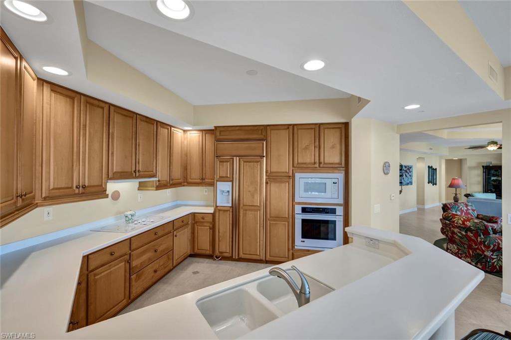 295 Grande Way, Unit 405 Naples, FL 34110 - Photo 14 of 40 a large kitchen with stainless steel appliances granite countertop a sink dishwasher a stove and a refrigerator with wooden cabinets