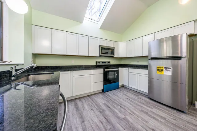 a kitchen with stainless steel appliances granite countertop a sink a stove a refrigerator with white cabinets and wooden floor