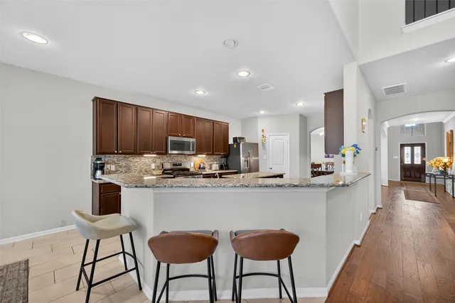 a kitchen with stainless steel appliances granite countertop a stove top oven a sink a refrigerator and white cabinets with wooden floor