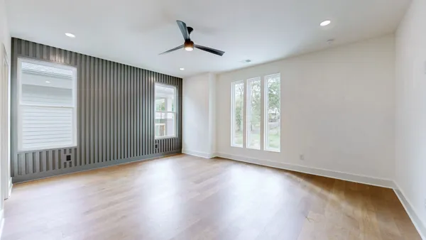 an empty room with wooden floor fan and windows