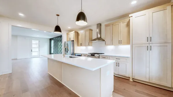 a kitchen with stainless steel appliances a stove a sink a refrigerator and white cabinets with wooden floor