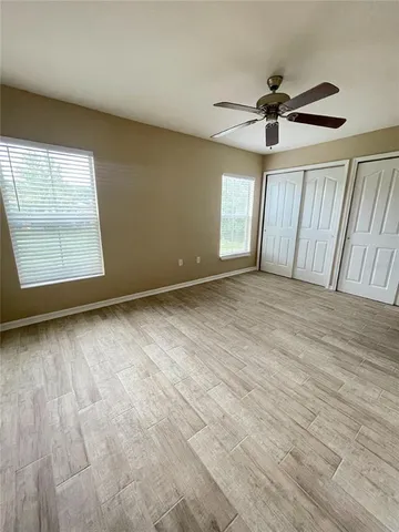 an empty room with wooden floor fan and windows