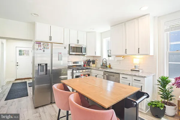 a kitchen with stainless steel appliances kitchen island granite countertop a refrigerator a stove a sink and white cabinets with wooden floor