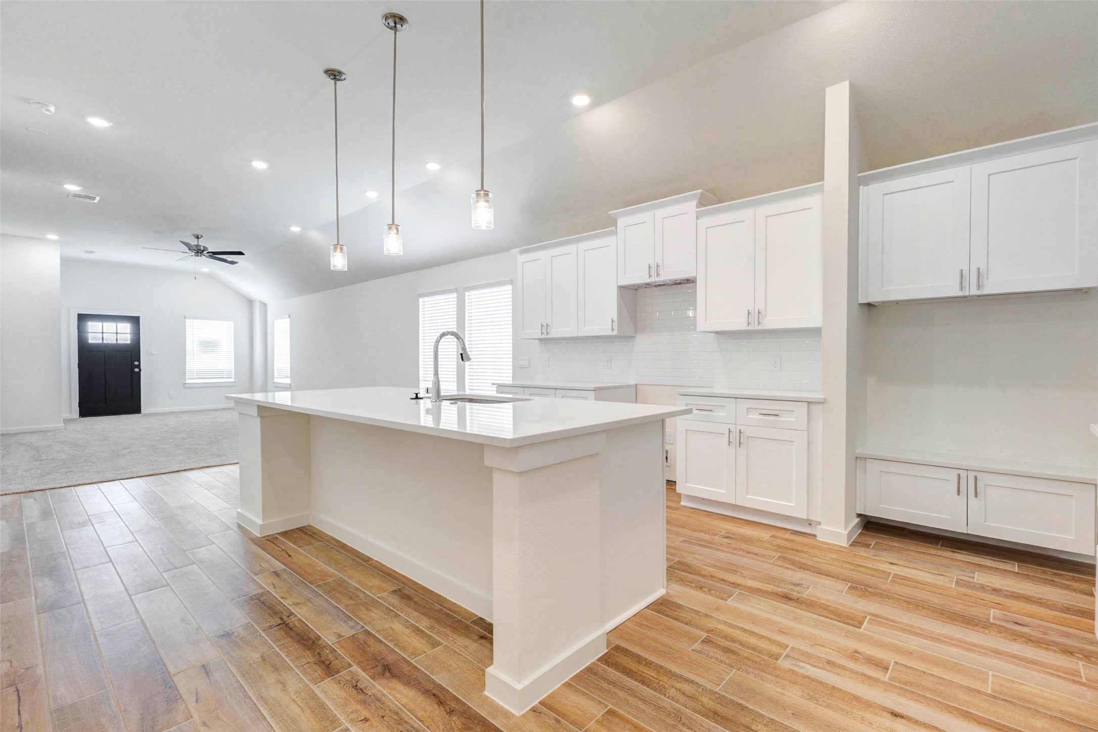 6463 Escondido Drive Rosharon, TX 77583 - Photo 12 of 30 Kitchen view showcasing the oversized island, white cabinetry, quartz counters, subway tile backsplash, pendant lighting, and open connection to the living room. The layout is designed for easy entertaining and comfortable everyday living.